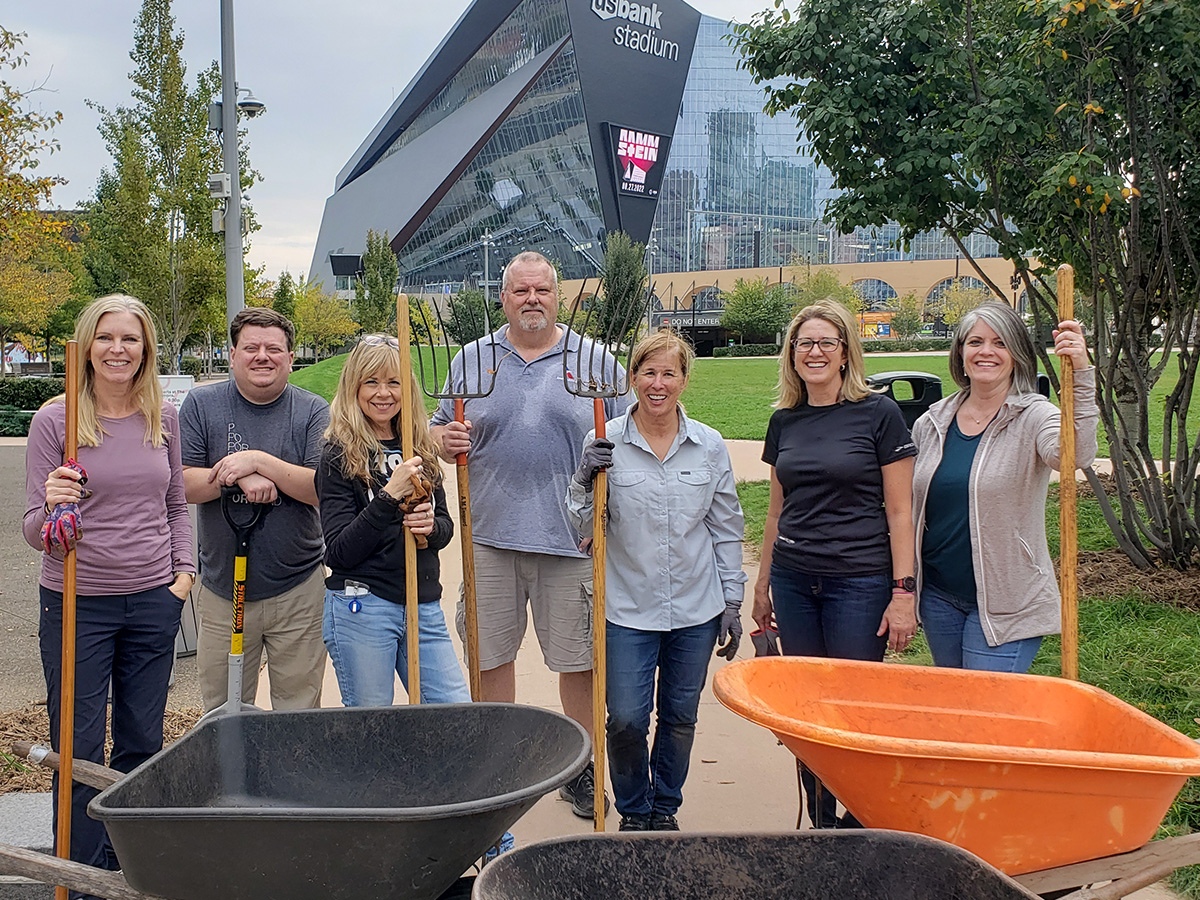 A group of people with rakes pose next to some wheelbarrows. 